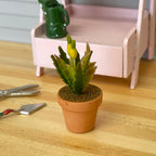 1:12 scale miniature spiky leaf plant with yellow buds in a terracotta clay pot, shown on a wood potting table
