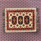 1:12 scale miniature woven area rug with fringe in cream and red with three medallions, shown on a pink brick surface