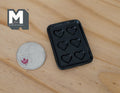1:12 scale miniature black resin heart cookie pan with 6 heart molds, shown on a wood surface beside a coin for scale