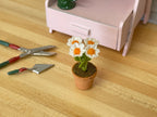 1:12 scale miniature potted white daisies in clay pot with orange centers, shown beside garden tools