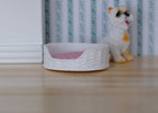 1:12 scale miniature pet bed in white with a pink cushion, woven look sides, shown beside a cat figurine