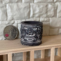 1:12 scale miniature black round planter in cast resin with white sailing ship relief, shown on a shelf beside a coin
