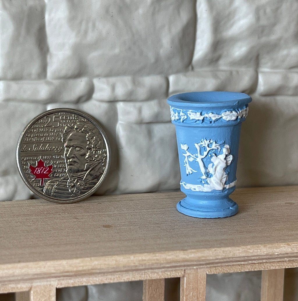 1:12 scale miniature trumpet vase in pale blue cast resin with white relief figures, shown beside a coin