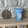 1:12 scale miniature trumpet vase in pale blue cast resin with white relief figures, shown beside a coin