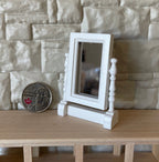 1:12 scale miniature swivel vanity mirror in white with turned posts, shown on a wood shelf beside a coin