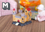 1:12 scale miniature wood toy castle with turrets and drawbridge door, yellow walls and red roof, shown by a baby doll