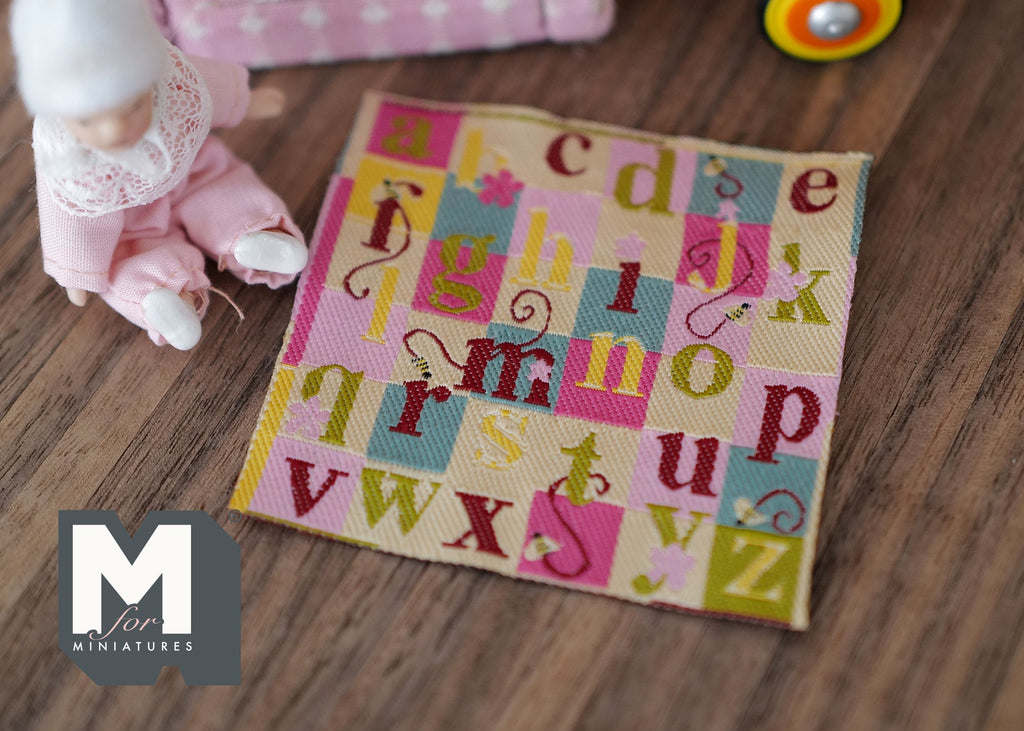1:12 scale miniature beige alphabet play mat with colorful letters in pink, yellow and teal squares, on a wood floor