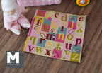 1:12 scale miniature beige alphabet play mat with colorful letters in pink, yellow and teal squares, on a wood floor