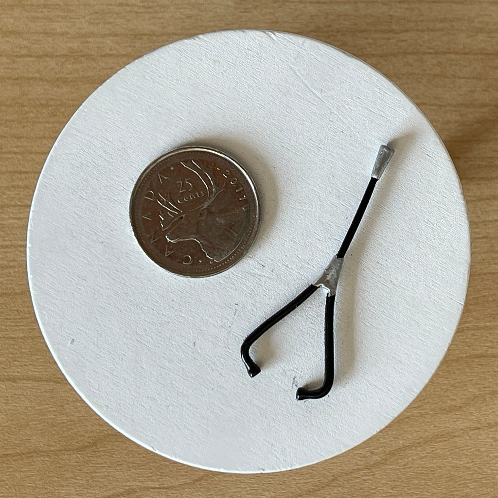 1:12 scale miniature black metal stethoscope with silver chest piece, shown on a white round base beside a coin