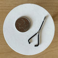 1:12 scale miniature black metal stethoscope with silver chest piece, shown on a white round base beside a coin