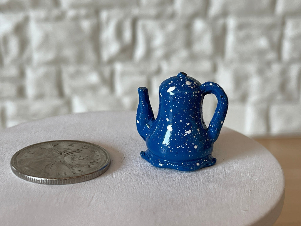 1:12 scale miniature cast metal teapot in dark blue with white speckles and fixed lid, shown beside a coin for scale