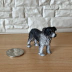 1:12 scale miniature black and white collie dog figurine, standing, shown on a wood floor beside a coin for scale