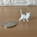 1:12 scale miniature unpainted kitten figure in white, walking pose with tail up, shown beside a coin