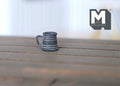 1:12 scale miniature metal tankard mug with handle in pewter gray with banded sides, shown on a wood plank table
