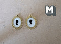 1:12 scale miniature silhouette portraits in oval gold frames, set of 2, black profiles on white, on a beige surface