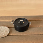 1:12 scale miniature black metal cooking pot with handles and lid, medium, shown on a wood table beside a coin