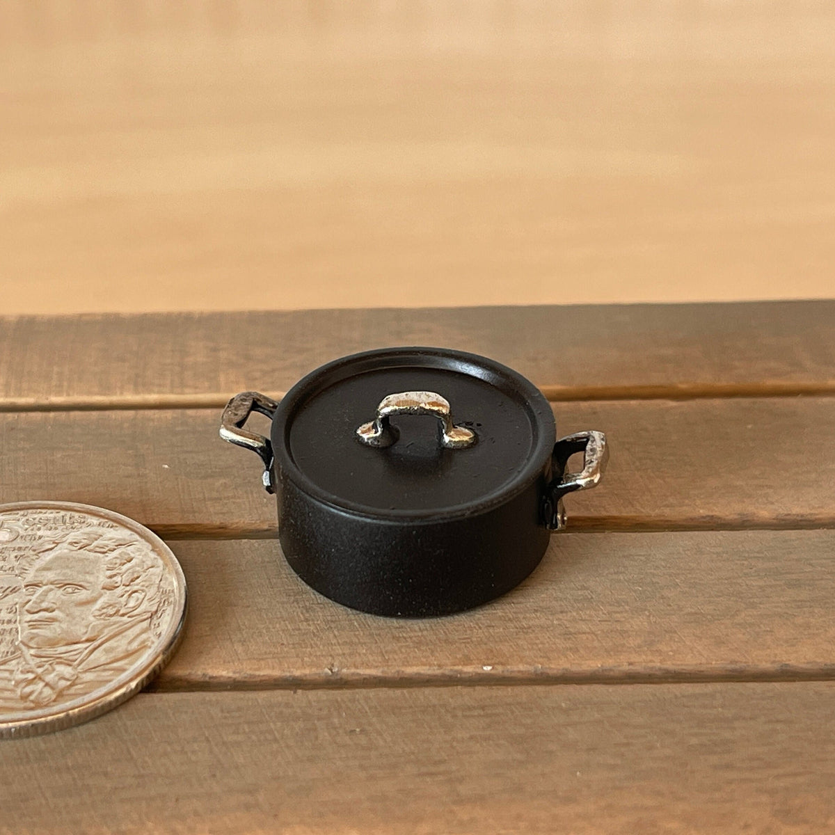 1:12 scale miniature black metal cooking pot with handles and lid, medium, shown on a wood table beside a coin