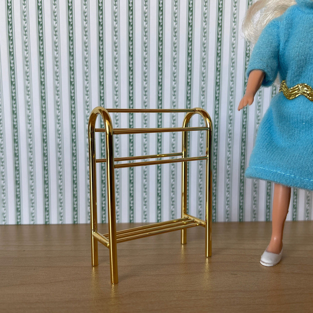 1:12 scale miniature metal quilt rack in gold with arched top and 2 bars, shown beside a doll in a blue dress