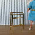 1:12 scale miniature metal quilt rack in gold with arched top and 2 bars, shown beside a doll in a blue dress