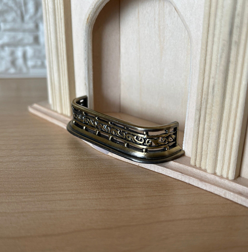 1:12 scale miniature metal fireplace fender in antique brass with curved ends, shown at an unpainted fireplace