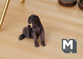 1:12 scale miniature sitting puppy figurine in dark brown scratching its ear, shown on a wood floor