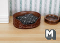 1:12 scale miniature wicker style pet bed in brown with black floral cushion, shown on a wood floor beside a bowl