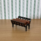 1:12 scale miniature metal fireplace log holder in black with brown logs, shown on a wood floor by striped wallpaper
