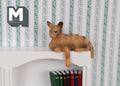 1:12 scale miniature ginger tabby cat shelf sitter with paws over the edge, shown lying on top of a white bookcase