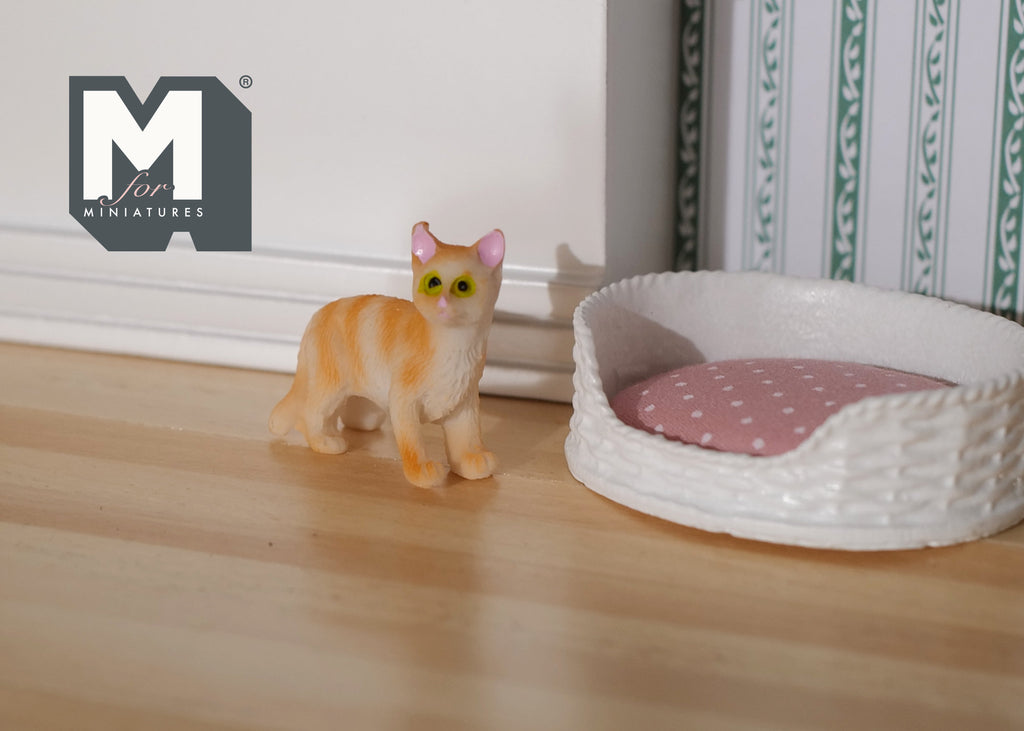 1:12 scale miniature standing orange tabby cat with white chest, shown on a wood floor beside a pet bed