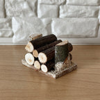 1:12 scale miniature wood log pile on base, stacked cut logs with bark, shown against a white stone wall
