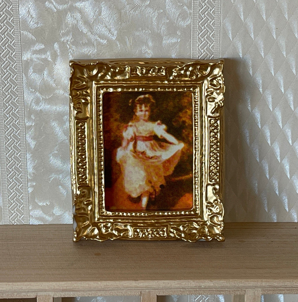 1:12 scale miniature portrait of a young girl in a white dress in an ornate gold frame, shown leaning on a wood shelf