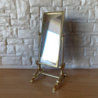 1:12 scale miniature metal cheval standing mirror in brass with tilting frame, shown by a white stone wall