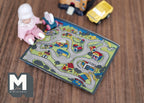 1:12 scale miniature town road play mat with printed streets and houses, shown on a wood floor with a baby doll and toy cars