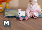 1:12 scale miniature rabbit pull toy with fixed wheels, white bunny on a teal base with pink wheels, on a wood floor