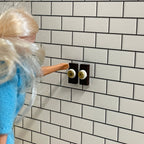 1:12 scale miniature round light switches with square dark plates, set of 2, non working, shown on a white tile wall
