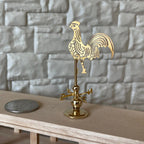1:12 scale miniature brass rooster weather vane on stand with compass arrows, shown beside a coin on a wood shelf