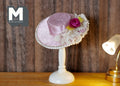 1:12 scale miniature boater hat in pink with lace and flower trim, fixed on a white hat stand, beside a lamp