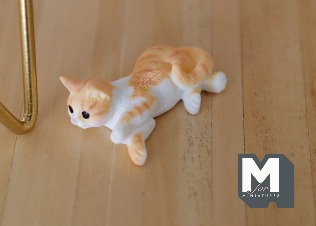 1:12 scale miniature lying cat in ginger and white, crouching pose, shown on a wood floor