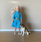 1:12 scale miniature sitting Saint Bernard dog figurine in brown and white, shown beside a doll for scale