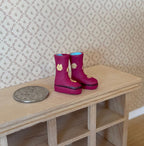 1:12 scale miniature pink rubber rain boots with yellow flowers, pair, on a wood shelf beside a coin for scale