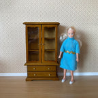 1:12 scale miniature wood dish cabinet in walnut with glass doors and 2 drawers, shown beside a doll for scale