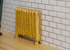 1:12 scale miniature gold antique style column radiator with ornate relief, shown against a white tile wall