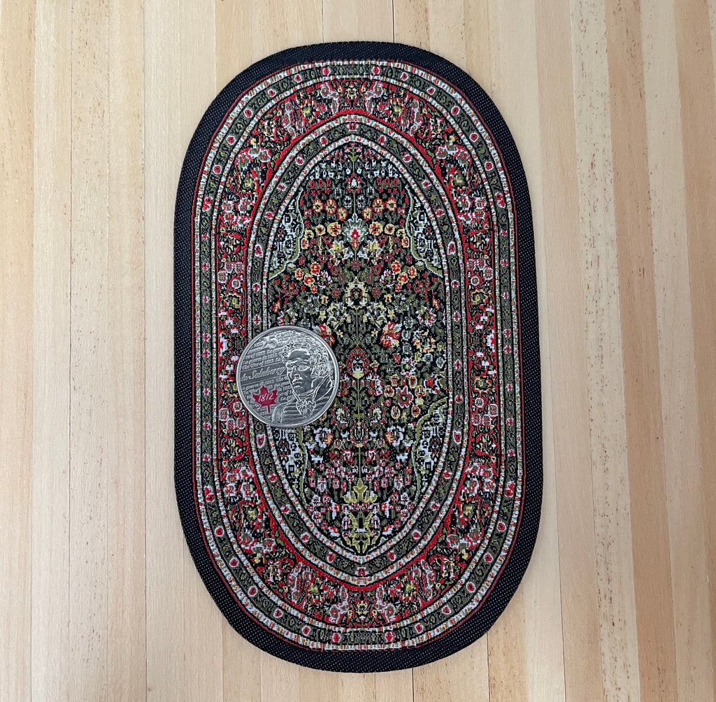 1:12 scale miniature oval area rug with floral medallion in red, green and black, shown on a wood floor with a coin