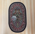 1:12 scale miniature oval area rug with floral medallion in red, green and black, shown on a wood floor with a coin