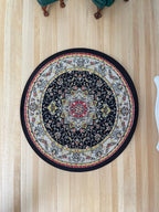 1:12 scale miniature round area rug in black with a Victorian style floral medallion and cream border, on a wood floor