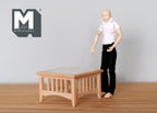 1:12 scale miniature unpainted wood coffee table, square with slatted sides, shown beside a poseable figure for scale