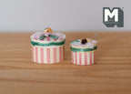 1:12 scale miniature striped hat boxes with floral lids, set of 2, pink and white stripes, shown on a wood surface