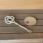 1:12 scale miniature metal rug beater in white with a looped knot head, shown on a wood table beside a coin