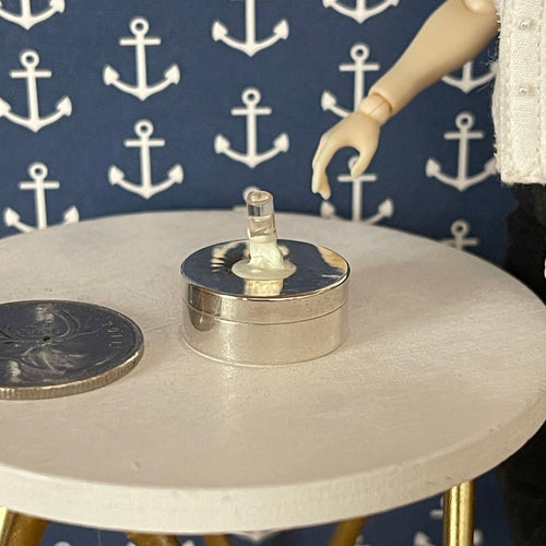 1:12 scale miniature battery powered LED light bulb on a round chrome base, shown on a table beside a coin