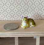 1:12 scale miniature lying tabby cat in tan with green eyes, style A, shown on a wood shelf beside a coin